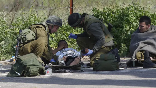 Un soldado isrelí herido recibe atención médica de varios compañeros después de que impactara un misil antitanques en su vehículo cerca de la zona de Har Dov