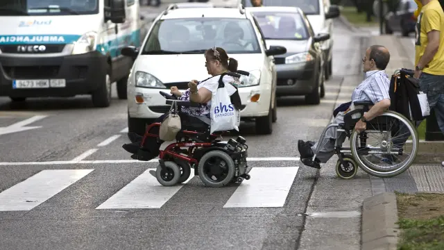 Dos zaragozanos atraviesan un cruce en silla de ruedas