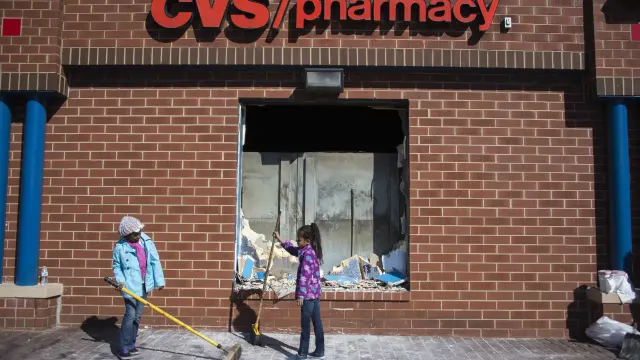 Dos mujeres limpian los destrozos en una farmacia de Baltimore.