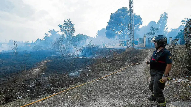 Un bombero sofoca los rescoldos de la vegetación quemada junto al colegio de Santa Ana.