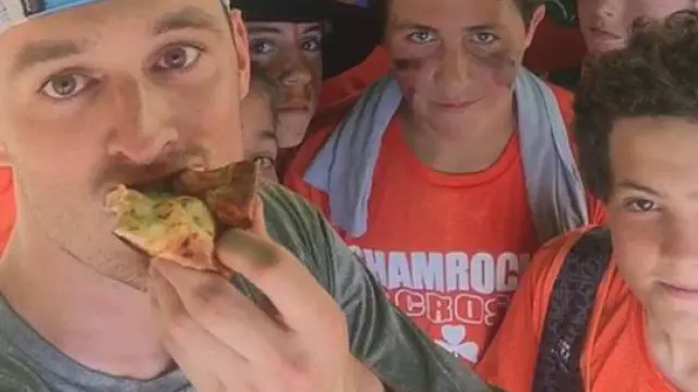 Kyle Feeney tomando una porción de pizza, rodeado de jóvenes.