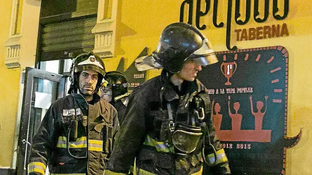 Dos bomberos salen del local tras sofocar el incendio.