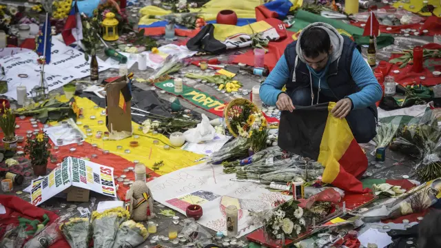 Un joven deposita una bandera de Bélgica junto a mensajes, flores y velas en homenaje a las víctimas.