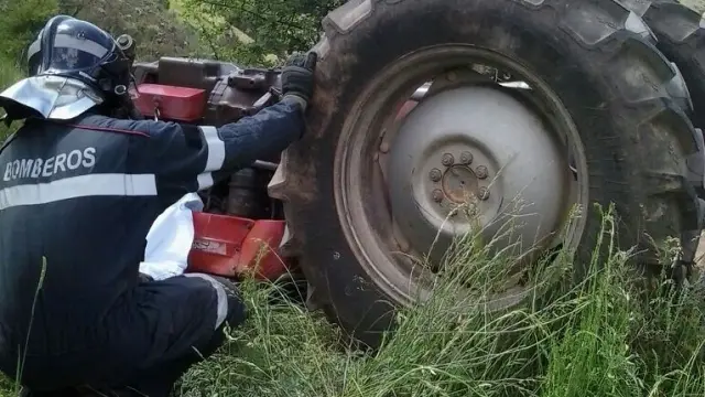 Imagen de unos bomberos, junto un tractor volcado