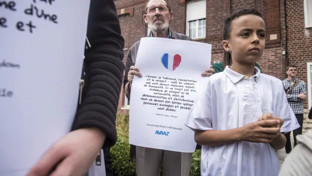 Varias personas sostienen pancartas en homenaje al párroco asesinado en Francia