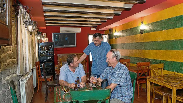 Santiago Rodríguez atiende a dos clientes en la cafetería de su hotel en Gea de Albarracín.
