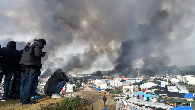 Varios inmigrantes ven parte del campamento ardiendo.
