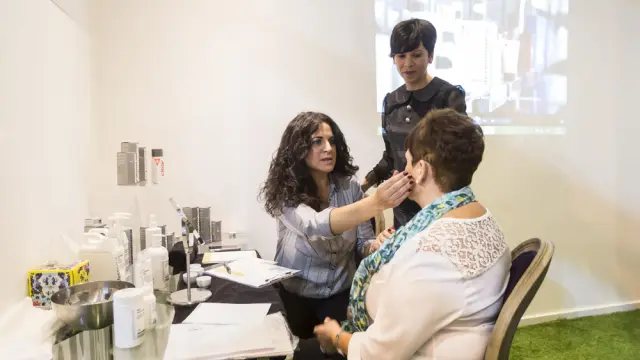 Eva Porroche, de pie, y Mari Carmen Valero, sentada, analizando por zonas la piel de una clienta mediante la técnica del ´face mapping`.