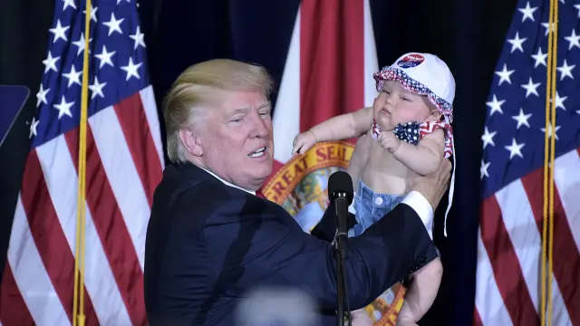 Trump sosteniendo a un bebé en un acto de campaña.