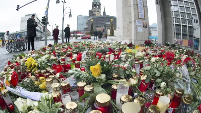 Varias personas pasan junto a las velas y las flores en la plaza Breitscheidplatz.