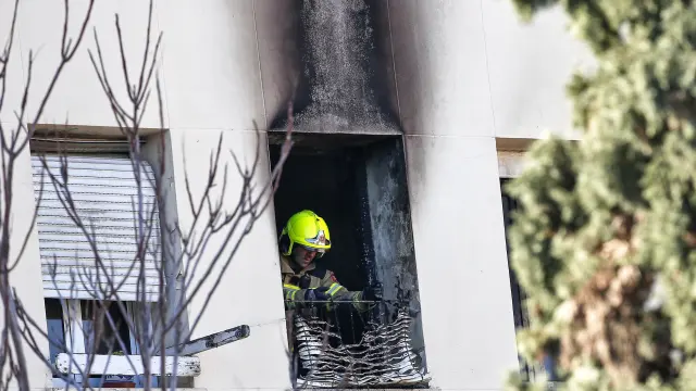 Un bombero retira una persiana quemada de la vivienda en la que este mediodía se ha declarado un incendio, en el que ha fallecido una mujer de 64 años al precipitarse desde un tercer piso.