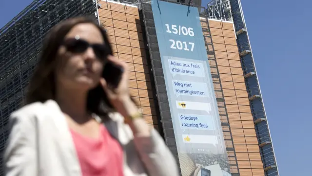 Una mujer habla por el móvil en Bruselas cerca de un cartel que habla del fin del 'roaming'.