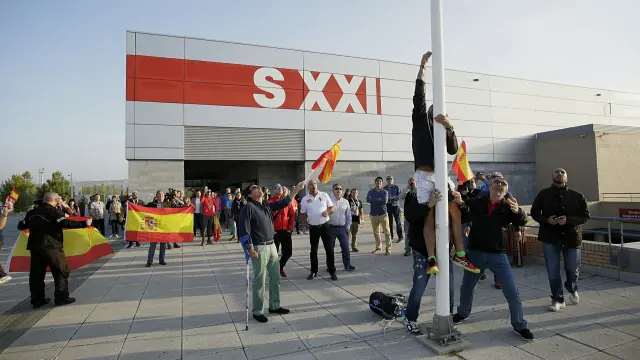 Varias personas han izado la bandera española a las puertas del pabellón siglo XXI.