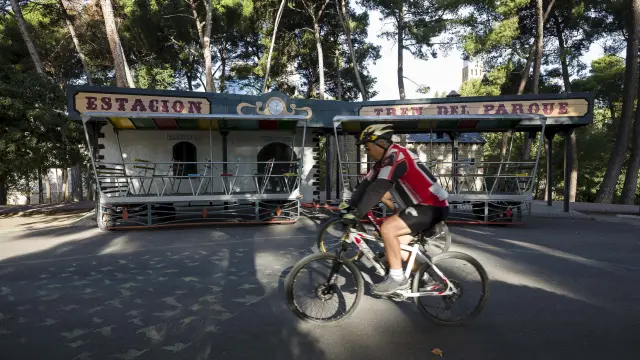 Un ciclista circula frente a la carrocería del tren chuchú del parque.