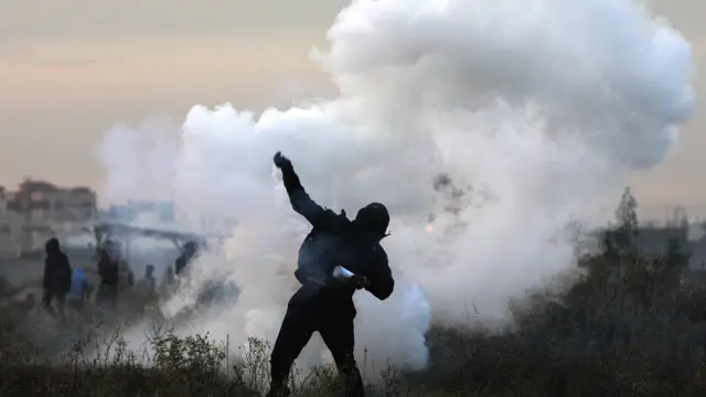 Un manifestante palestino devuelve una granada de gas israelí durante los enfrentamientos en la Franja de Gaza
