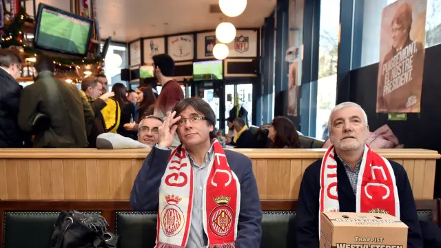 Puigdemont, con la bufanda del Gerona, sigue el partido de fútbol en un bar de Bruselas.