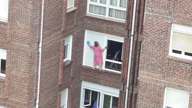 La mujer limpia la persiana apoyada completamente en el alféizar de la ventana.