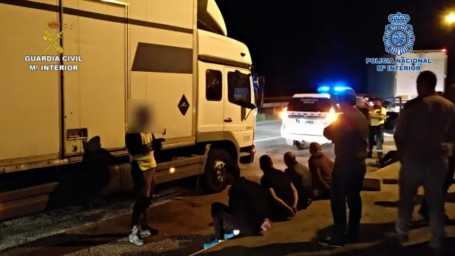 Varios de los detenidos, sentados en el suelo y vigilados por agentes de la Guardia Civil y la Policía Nacional.
