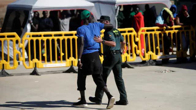 Un inmigrante rodea con el brazo a un guardia civil que cuida y vigila a las personas que llegan en patera a las costas de Cádiz y son trasladadas al pabellón 'Antonio Gavira', en el municipio Los Barrios, cerca de Algeciras.