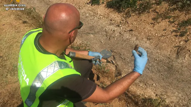 Un agente de la Guardia Civil sostiene un ave muerta junto al lugar donde se ha denunciado el vertido ilegal al río.