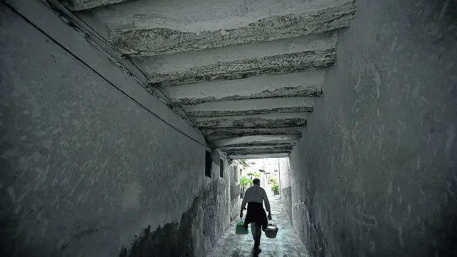 Un vecino de Sabiñán, cargado con dos cubos, camina por el florido callejón que conduce a su residencia.
