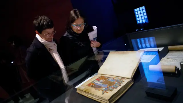 Dos visitantes observan el Gran Libro de los Feudos, una de las joyas del Archivo de la Corona de Aragón que se exhiben en Barcelona.