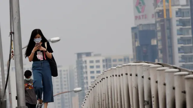 Una joven lleva mascarilla mientras cruza un paso elevado en Bangkok (Tailandia) debido a la alta contaminación atmosférica.