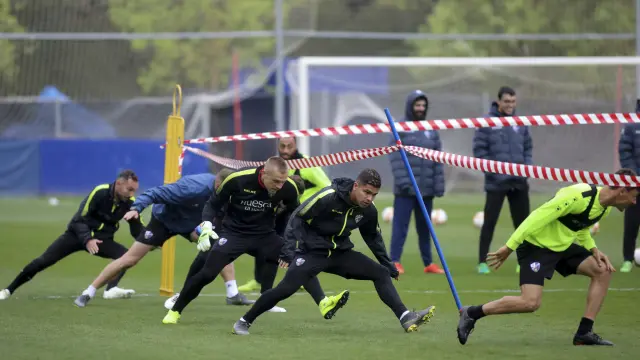 Varios jugadores del Huesca pasan por debajo de una cinta durante un ejercicio.