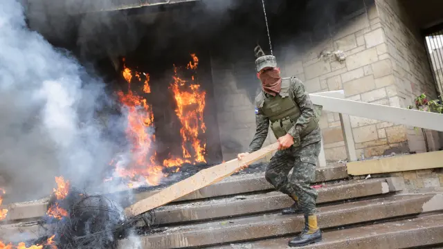 Un soldado intenta apagar los neumáticos en llamas en una de las puertas de acceso a la Embajada de Estados Unidos.