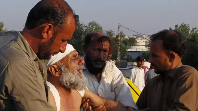 Varias personas ayudan a trasladar a un herido en el accidente áereo ocurrido en una zona de viviendas de Rawalpindi (Pakistán).