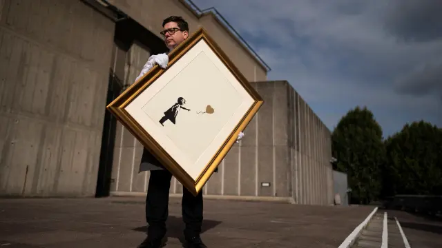 London (United Kingdom), 30/08/2019.- A Christie's employee poses with a print of the gold version of 'A Girl with Balloon' artwork by anonymous British street artist Banksy on the Southbank in Central London, Britain, 30 August 2019. Two versions of the artwork will be sold at a dedicated Christie's online sale of Banksy's work called 'Banksy: I can't believe you Morons actually buy this sh*t' from 11 to 24 September. (Reino Unido, Londres) EFE/EPA/WILL OLIVER Christie's photocall with A Girl with Ballloon artwork in London