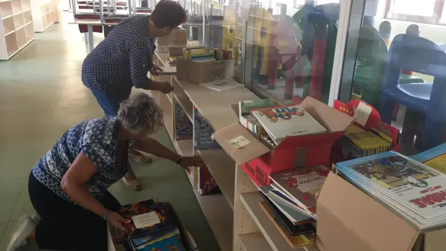 Dos voluntarias ordenan algunos de los libros infantiles en las nuevas instalaciones.