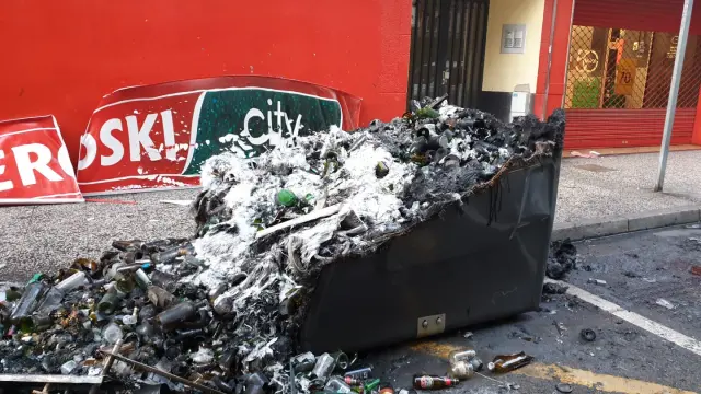 Los restos de los contenedores quemados este domingo por la mañana. El fuego ha afectado a la fachada de un supermercado, dos motos y una vivienda.