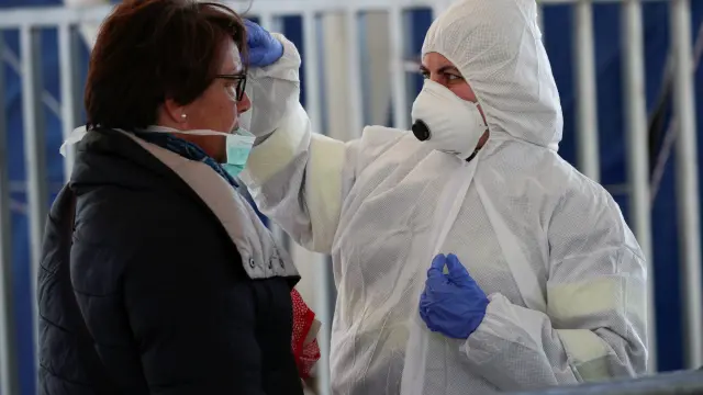 A person wearing a protective suit and mask checks the temperature of people departing from the ferry port of Molo Beverello after Italy orders a countrywide lockdown to try and contain a coronavirus outbreak, in Naples
