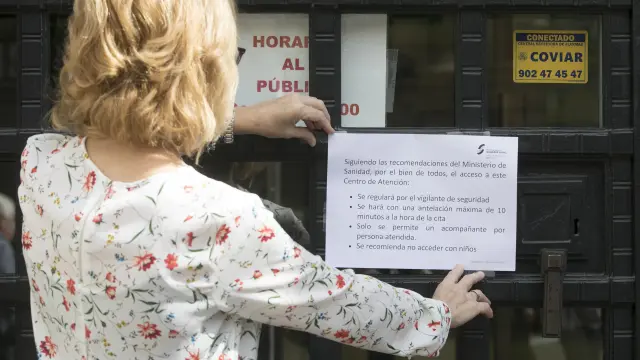 Una funcionaria del INSS coloca en la puerta de la oficina de la calle de Joaquín Costa de Zaragoza el cartel que explica las medidas adoptadas.