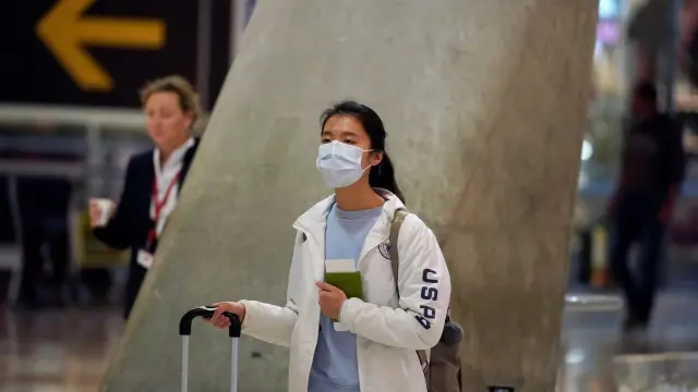 A passenger, wearing a protective mask, walks to check-in for her flight to the U.S. at Madrid's Adolfo Suarez Barajas Airport