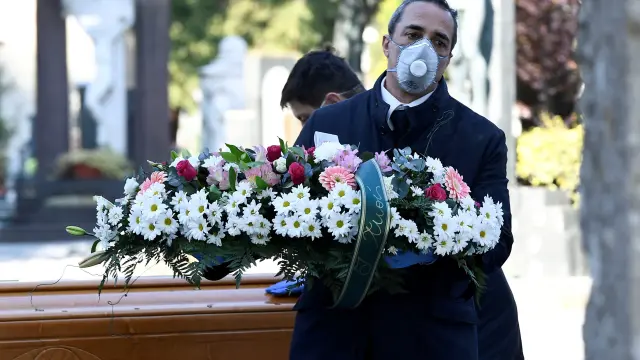 Un trabajador de una funeraria transporta una corona de flores en un cementerio de Bérgamo, en Italia.