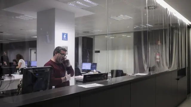 Un funcionario, atendiendo el teléfono detrás del mostrador del juzgado de guardia de Zaragoza, protegido con una cortina de plástico.
