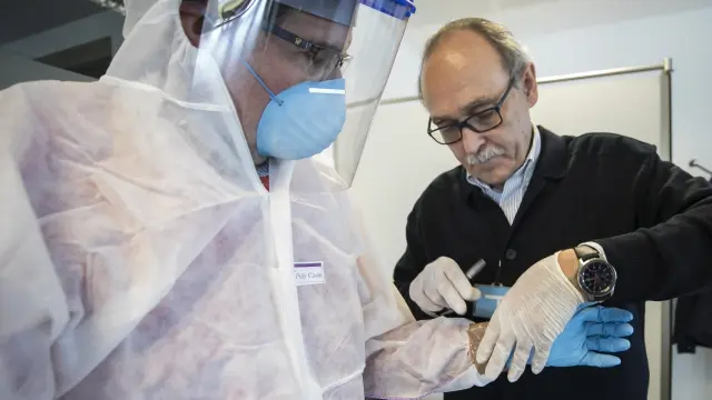 El director del Instituto de Medicina Legal de Aragón, José Manuel Arredondo, ayuda a su colega Salvador Baena a ponerse el equipo de protección.
