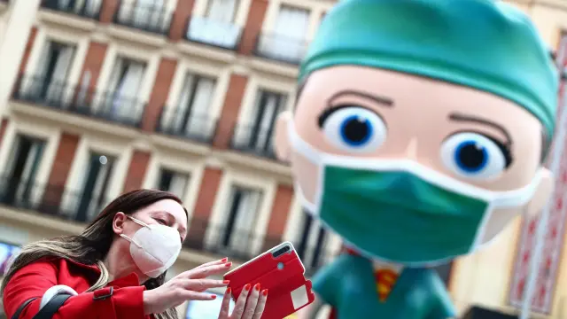 A woman wearing a protective face mask takes a selfie next to an oversized model of a health worker in Madrid