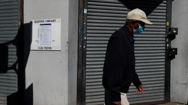 A man walks with a protective face mask past a closed library amid the coronavirus disease (COVID-19) outbreak in the Far Rockaway section of the Queens borough of New York