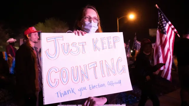 Schmidt holds sign giving encouragement to election workers among "Stop the Steal" protesters in North Las Vegas