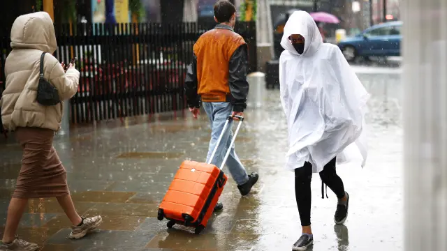 A person wearing a poncho and protective face mask walks through heavy rainfall, amid the coronavirus disease (COVID-19) outbreak, in London