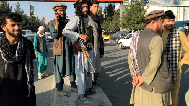 A member of Taliban stands guard as people walk at the entrance gate of Hamid Karzai International Airport in Kabul, Afghanistan, August 16, 2021.REUTERS/Stringer[[[REUTERS VOCENTO]]] AFGHANISTAN-CONFLICT/
