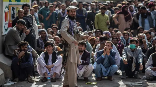 Un talibán, delante de un grupo de hombres que esperan que abra un banco para sacar dinero, en Kabul
