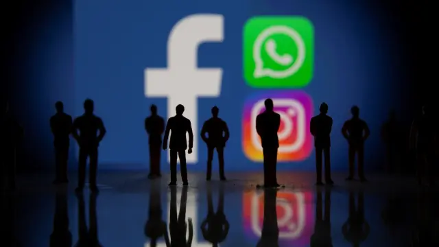 Small toy figures are seen in front of displayed Facebook, Whatsapp and Instagram logos in this illustration