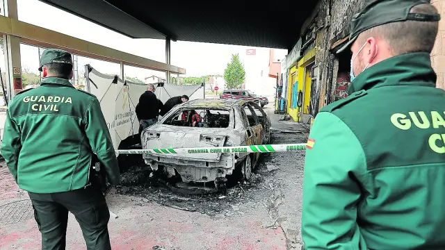 Dos guardias civiles custodian el coche consumido por las llamas en la gasolinera de Mora de Rubielos.