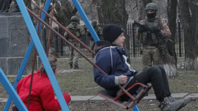 Niños ucranianos en un parque ante la mirada de un soldado ruso en en Lugansk.
