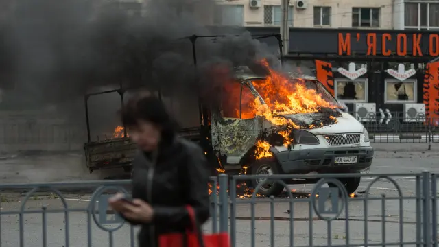 Una mujer camina delante de una furgoneta ardiendo alcanzada por un misil en Járkov