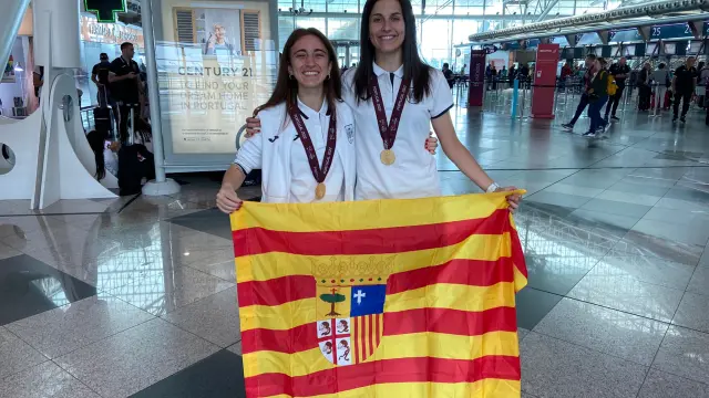 Irene Samper y María Sanz posan con la bandera de Aragón y las medallas de campeonas de Europa en el aeropuerto de Oporto.